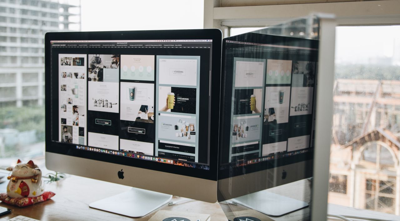 services-01 Dual monitors on a desk, showcasing web design in a modern office setting.