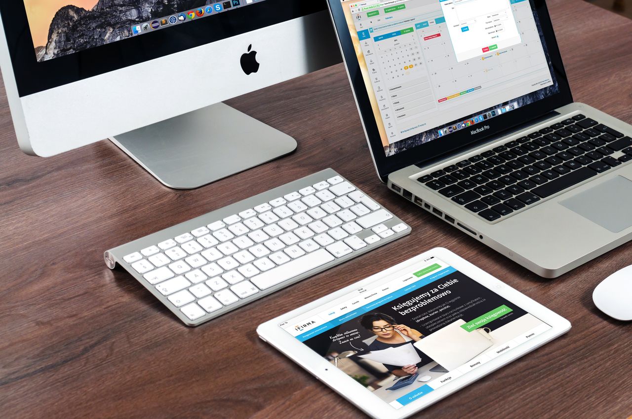 services-02 A sleek office desk setup featuring Apple devices: iMac, MacBook, and iPad.
